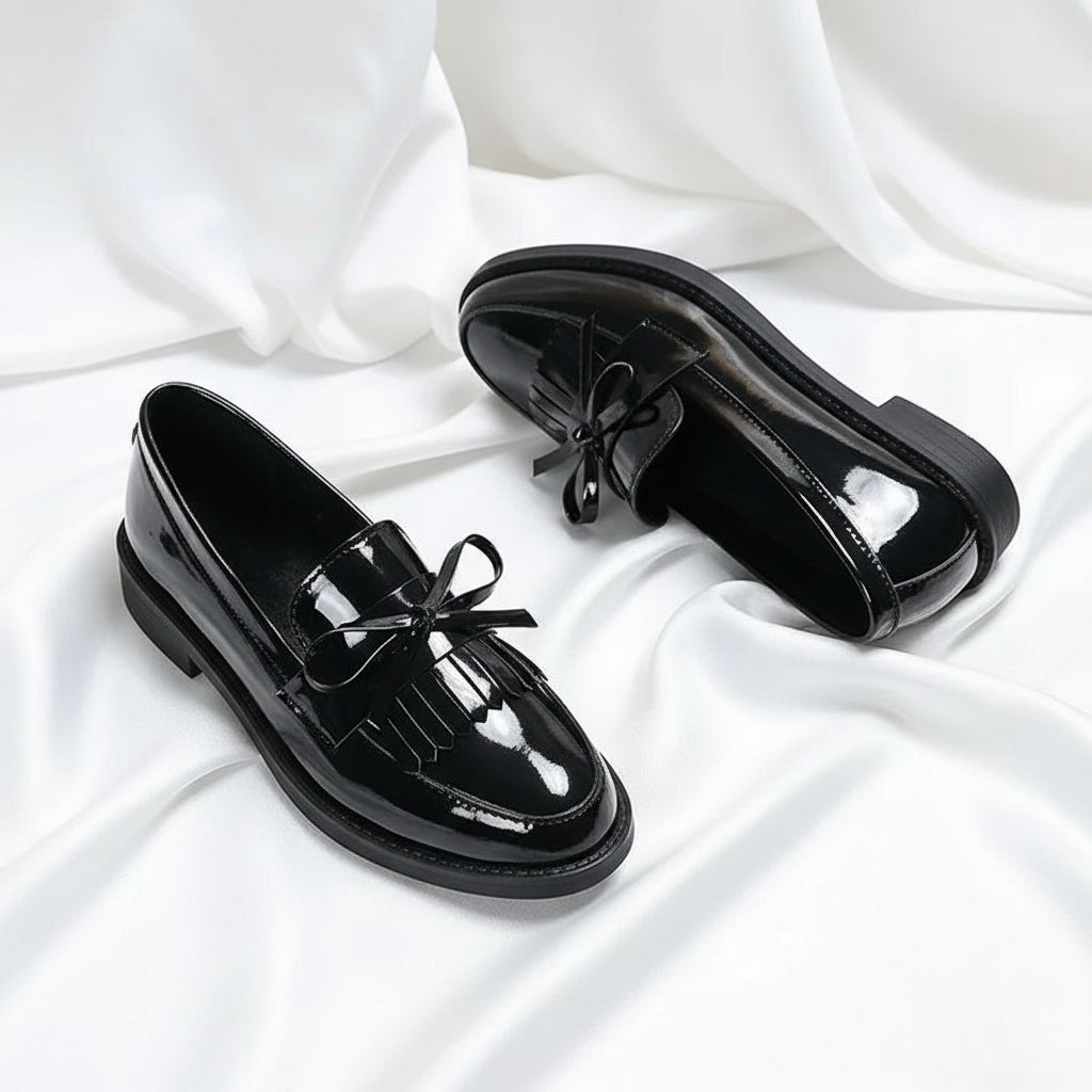 Black patent leather shoes with bow details on a white background
