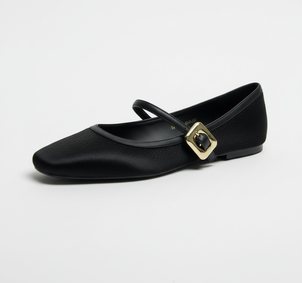 Black flat shoe with a gold buckle on a white surface and beige background