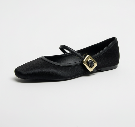 Black flat shoe with a gold buckle on a white surface and beige background